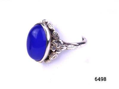 Arts & Crafts ring by Bernard Instone. Hallmarked silver ring set with bright sea blue oval chalcedony stone to centre and floral motifs to the shoulder either side. Size N / 6.5 Photo of side image of ring showing flower and leaves design on silver shoulders of ring