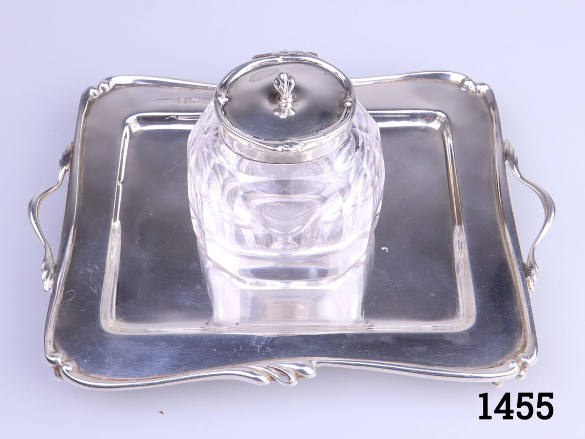 c1907 Birmingham assayed sterling silver and cut glass inkwell and stand. Inkwell sits securely in the hole in the centre of the stand. Inkwell weighs 190.6grams and measures 52mm x 45mm and 70mm tall. Stand measures 150mm long (including handles) and 110mm wide and weighs 95grams Photo looking down at inkwell on stand from a slight raised angle