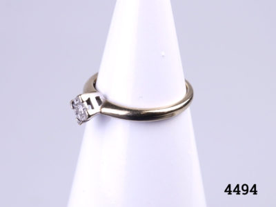 Vintage 9 karat gold ring with a small round cut diamond set on a white gold head.  Ring size M / 6. Ring weight 1.8 grams. Photo of ring on a display stand and seen from a slight side angle