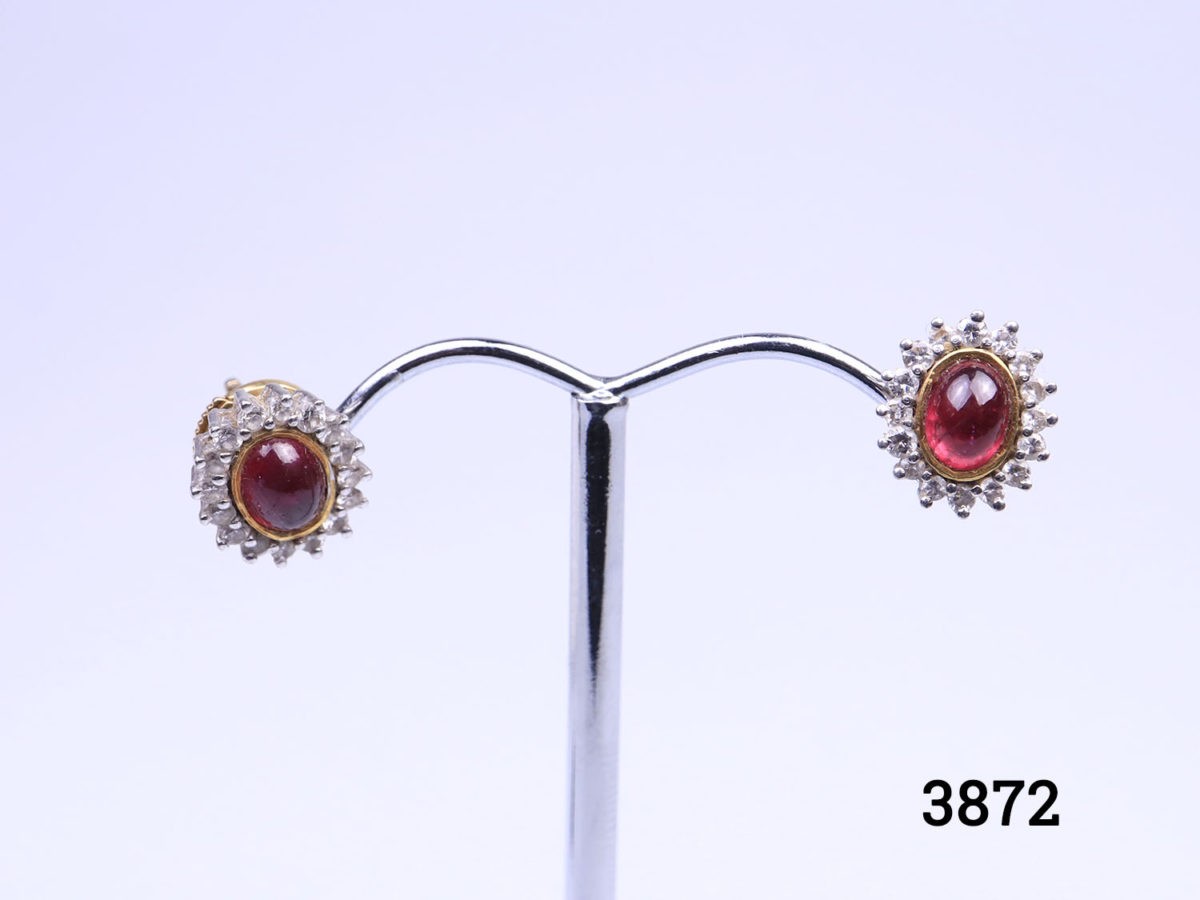Modern 18 karat gold stud earrings each set with ruby cabochon and round cut diamonds. Front of earrings measure 11mm by 9 mm. Earrings weight 4.1 grams. Box included. Photo of both stud earrings displayed on a stand