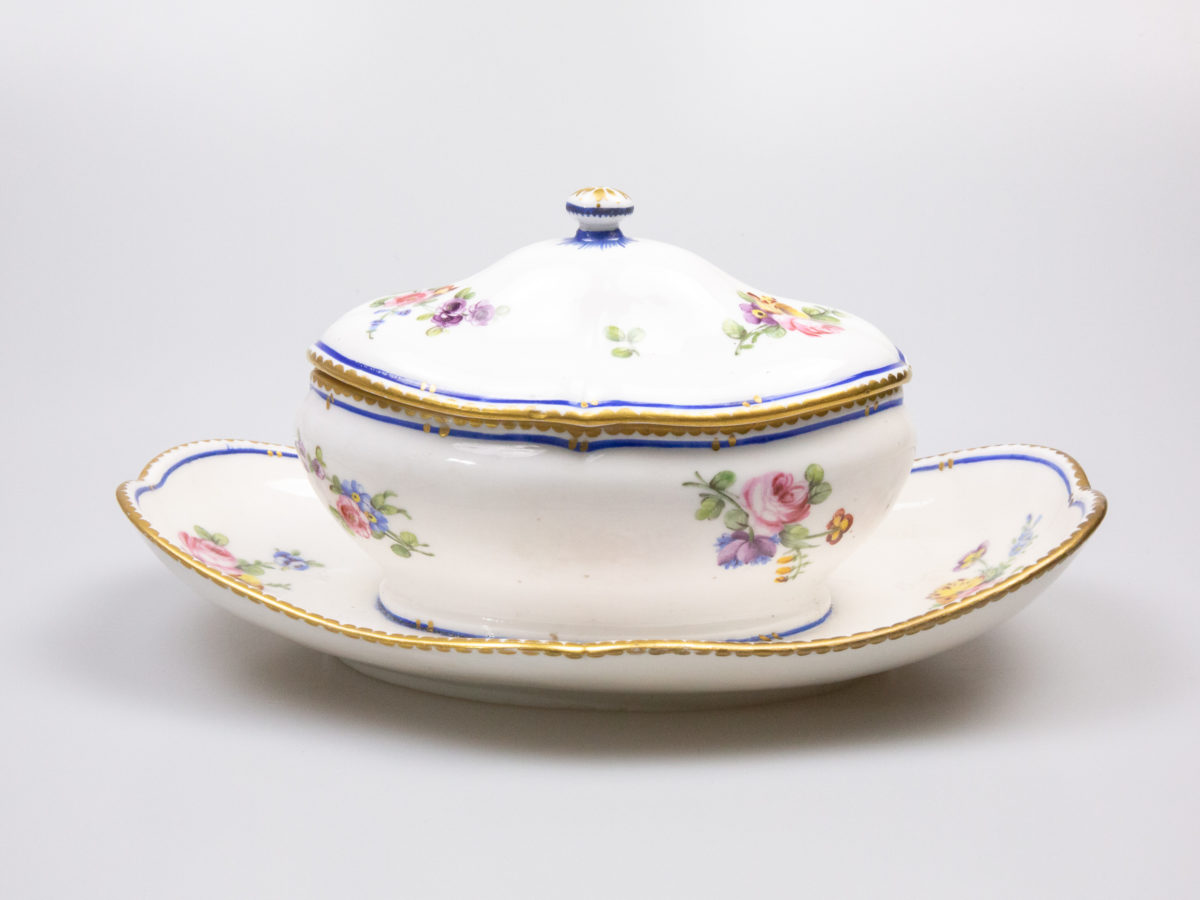 18th Century Sevres sauce boat. Soft paste porcelain sauce boat hand-painted in the feuille de choux pattern. Hairline crack to the inside of the sauce boat which does not come through under the plate. Interlaced L mark of Sevres to the base with double letter a denoting 1778. Photo of boat with lid in place and seen from a slight off side angle