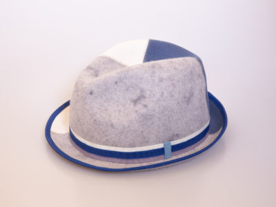 Modern 4 tone trilby hat. Unusual quirky trilby in a patchwork of colours. Size slightly adjustable with a clever Velcro strip on the inner band of hat. Outer material 100% wool. Inside band 100% polyester. Photo of left & front side of hat showing the pale grey patchwork block