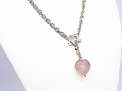 Kit Heath sterling silver and rose quartz necklace. Nice solid silver chain with an attached silver heart and a detachable rose quartz heart. The silver attachment bar is made to resemble an arrow. Rose quartz is believed to attract love and connects to the heart chakra. Detachable heart drop length is 47mm, full drop length of whole pendant area is 53mm. Hallmarked to the clasp, the attached heart and bar of detachable pendant. Close up photo of the rose quartz heart area of necklace.