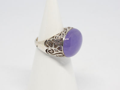 Modern sterling silver and lilac jade ring. Lovely ring with a large oval lilac jade stone set widthways to fit across the finger . Intricate scrollwork design to the silver on shoulders, gallery and bridge, Stone/ring front measures approximately 20mm by 15mm. Ring size R / 8.5. Ring weight 8.1gms. Photo of ring on a cone shaped display stand and seen with ring front facing right of picture.