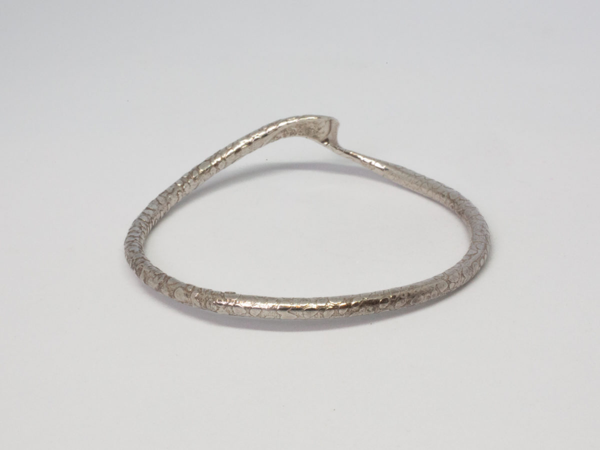 Modern sterling silver snakeskin bangle. Unusual bangle with snakeskin like pattern and a flat twist on one area giving a double snake like appearance. Fully hallmarked for London assay c2015. Inside diameter measures 65mm. Photo of bangle on flat surface with 'head and tail' end in the background.