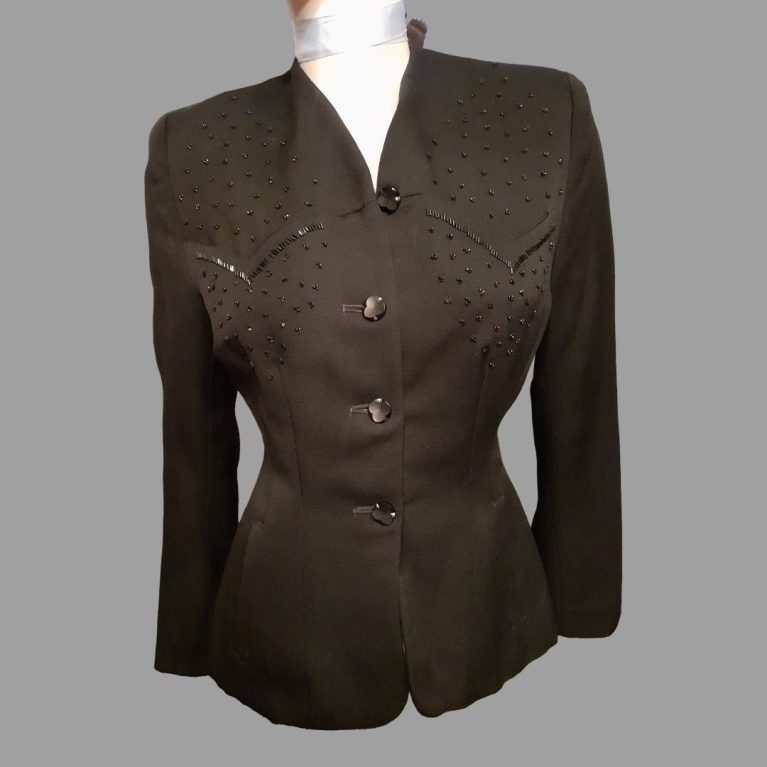 1940s black fitted jacket with bead embellishment on front. In excellent condition. Size 10. Main photo showing the jacket with buttons fastened from the front. The jacket has padded shoulders and a fitted waist area.