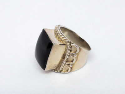 Vintage sterling silver and black onyx ring. A nice chunky sterling silver ring set with a large rectangular black onyx. Silver twist work frames the stone area. Hallmarked 925 for sterling silver. Stone measures 16mm by 12mm.  Ring size N.5-O / 7. Photo of ring on a flat surface and shown with ring front facing left and hi-lighting the decorative shoulder & frame.