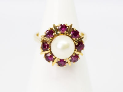 Vintage 14 karat gold ring with pearl and rubies. Pretty ring with a central pearl framed by 8 round cut rubies in a star/sun burst design on an open prong cathedral setting. Ring size N.5 / 7. Ring weight 5.6gms. Main photo of ring displayed on a cone shaped stand and seen with ring front facing forward.