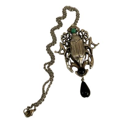 Art Nouveau style beetle necklace. Unsigned white metal necklace with an Art Nouveau style beetle pendant. The beetle is accentuated with a green bead at its head and black beads at its hind legs. A lovely statement piece. The pendant measures 85mm long and 55mm at widest point. Main photo of entire necklace with pendant to the right and chain laid to the left.
