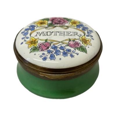 Vintage enamel box by Crummels & Co with a green pot base and floral design to lid with "Mother" to the centre. Floral design continues on inside of lid with a basket of flowers. Measures 44mm in diameter at base & top. Main photo of box seen from a slightly raised angle showing the design on the lid and green enamel to the sides.