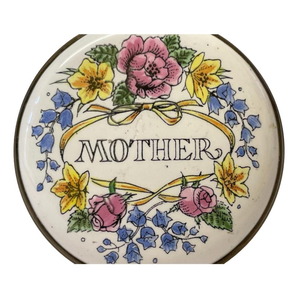 Close up photo of the decoration on the top of lid. Mother to the centre and flowers all around.