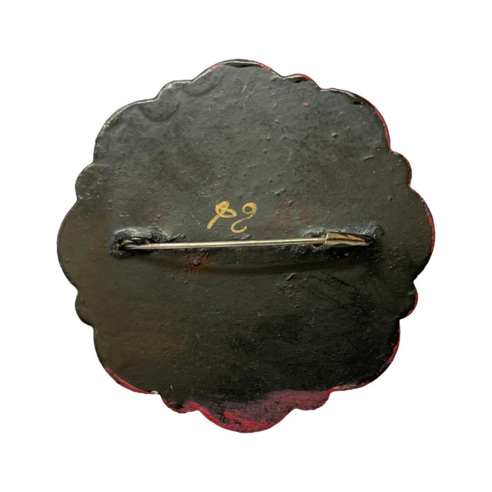Photo of back of brooch with pin closed. Artists mark visible.