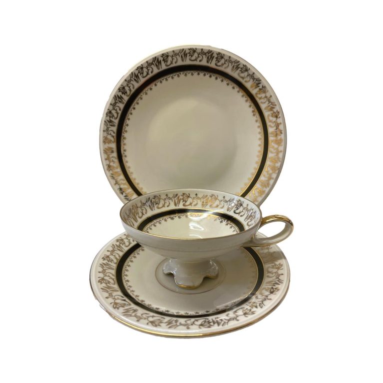 Main photo of Tirschenreuth porcelain Deco trio displayed with the cup cup in the saucer and placed in front of the small plate which is upright on a stand behind. The photo is taken from a slightly raised angle so peering into the cup a little. Each piece has a cream base colour with a border of an abstract floral design around the edge followed by a line in black and a second line of smaller abstract floral line to the inside below the black. The 4 fluted feet of the cup gives this piece an extra appeal.