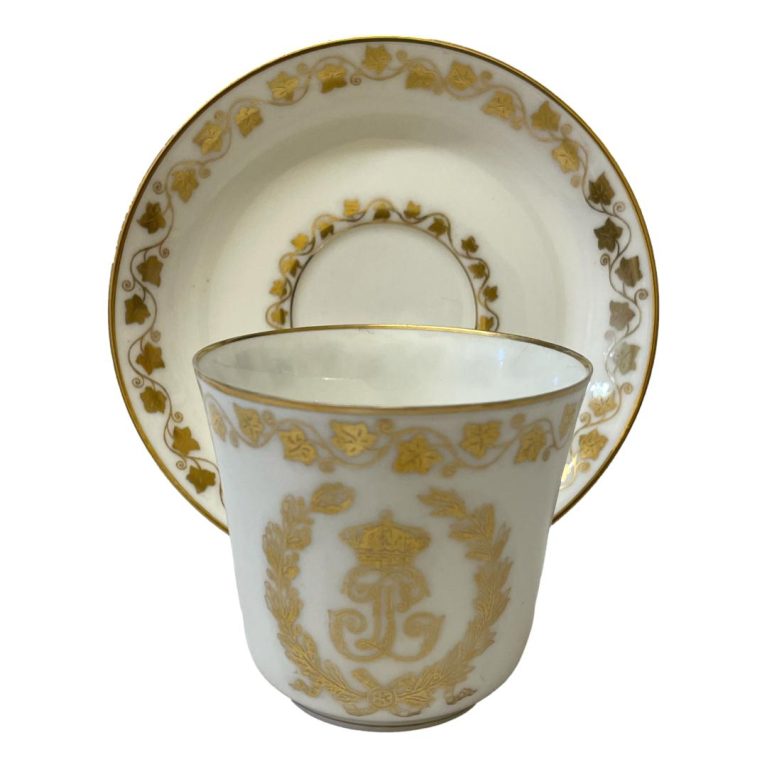 Main photo with cup placed in front of the saucer which is displayed upright on a stand. The decorated side of cup (opposite end to handle) is shown.