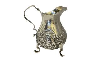 Antique sterling silver cream jug. Small & sweet cream jug in sterling silver on tripod feet with raised floral decoration to the sides and an empty cartouche to the jug breast for personalisation. Fully hallmarked to the side for Birmingham assay c1898. Main photo of jug seen from an eye level with handle to the left and spout to the right of photo. Only 2 of the 3 feet are visible.