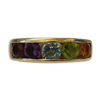 9 karat gold rainbow ring. A more modern ring in 9 karat gold set with 5 semi precious gem stones. The stones are set in a rainbow like formation with amethyst, garnet, aquamarine, peridot and citrine. Ring size R / 8.5. Ring weight 4.5gms. Main photo of ring on a flat surface and seen with from an eye level with ring front forward facing.