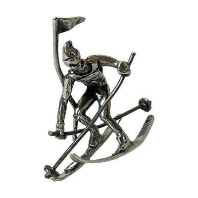 Sterling silver figurine of a skier. A modern miniature silver figurine of a skier in action pose on a slalom skiing course weaving around a flag. Incredible detailing makes for a very realistic pose. 925 hallmark to one ski and made in Italy. Measures 52mm long, 26mm at widest and 42mm at tallest. Weight 15.5 grams. Main photo of figurine seen from a forward facing angle. One ski pole is in front and other is behind. The action pose appears to have fluid movement.