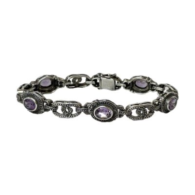 Sterling silver bracelet with marcasite and amethyst. Modern bracelet in an Art Deco style with 5 panels set with oval cut amethyst and each separated with a marcasite panel. Box clasp closure with added loop and ball hooks for added security. Hallmarked 925 to the clasp. Main photo of bracelet seen laid out in a circle on a flat surface with the amethyst and marcasite panels visible in the foreground and clasp area to the back.