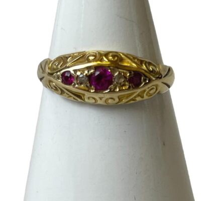 18 karat gold ring with rubies and diamonds. Pretty Victorian ring in 18 karat gold with 3 small round cut rubies & 2 tiny diamonds. Full hallmark to inside band for Birmingham assay. Date stamp very worn. Ring size N.5 / 7. Main photo of ring displayed on a cone shaped stand with ring front facing forward.