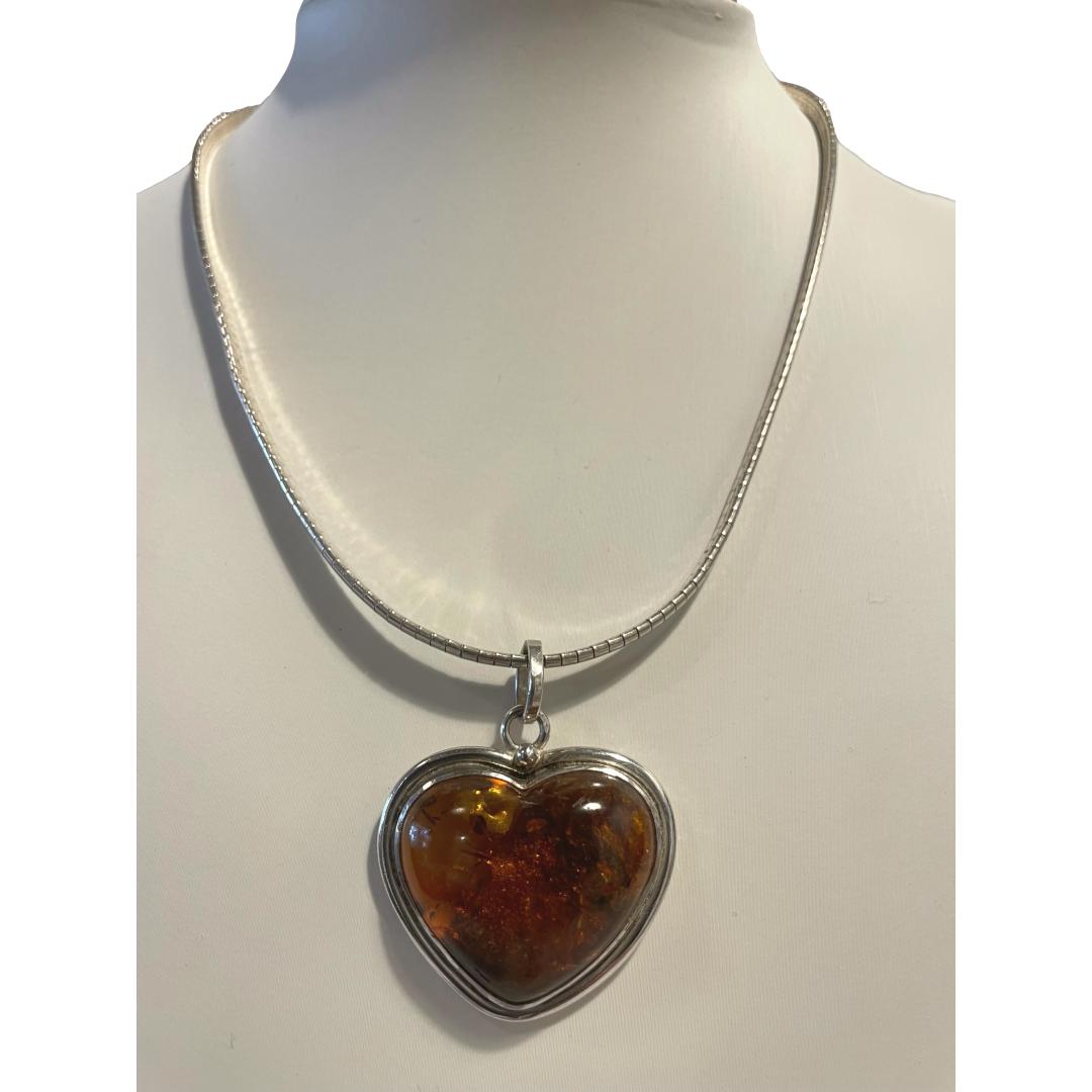 Sterling silver and amber heart pendant and chain. Modern sterling silver heart shaped pendant with heart shaped amber to the centre on a flat snake chain which holds the pendant perfectly. Hallmarked 925 to the pendant bail and 925 Italy to the chain clasp. Pendant measures 42mm long from top of bail and 35mm at widest. Main photo of necklace displayed on a stand and seen forward facing straight on.