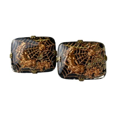 Unusual spiders web cufflinks. Art Nouveau inspired cufflinks of a spider in its web and a long haired maiden sitting on the outer edge with roses. The colouring of bright copper of the spider, web & maiden against the black enamel make these cufflinks stand out all the more. Set on a brass fixing. There is some wear to the black enamel which seems to add more effect to the image. Main photo of both cufflinks displayed with decorative images forward facing. The cufflink on the left is slightly set back. The contrast of black background and copper coloured design is very striking.