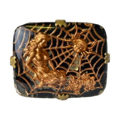 Unusual spiders web cufflinks. Art Nouveau inspired cufflinks of a spider in its web and a long haired maiden sitting on the outer edge with roses. The colouring of bright copper of the spider, web & maiden against the black enamel make these cufflinks stand out all the more. Set on a brass fixing. There is some wear to the black enamel which seems to add more effect to the image. Close up photo of one cufflink showing the details of the decorative design. The spider is in its web to the top right. The web extends to the whole cufflink front. The lady is reclining on the left hand side with flowers decorating the lower half of the web.