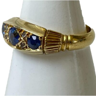 Antique 18 karat gold, sapphire & diamond ring. Antique Art Deco ring with 3 round cut sapphires each separated by 2 small round cut diamonds. Fully hallmarked to inside band for Chester c1914. Ring size K / 5.25. Photo of ring on cone shaped stand and seen with ring front facing towards the left showing the shoulders.