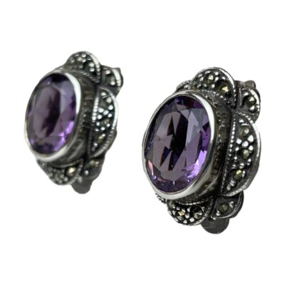 Vintage clip-on earrings with amethyst. Sterling silver clip-on earrings with a good sized oval cut amethyst stone to the centre with marcasite surround. Hallmarked 925 for sterling silver to the back. Both clips in good working order. Earrings measure 20mm long by 16mm wide. Amethyst measures 10mm by 8mm. Photo of earrings seen from a side view and in close up. The amethyst fronts are facing towards the left.