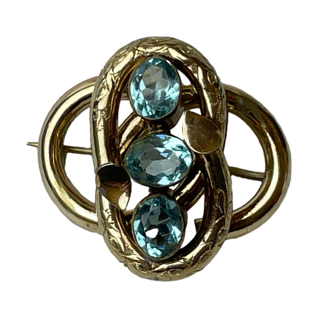 Victorian brooch with faux aquamarine. A striking Victorian pinchbeck brooch set with 3 pale blue oval cut faux aquamarines. Lovely metal working of the brooch frame in an intertwined figure of eight like pattern. Main photo of brooch seen from the front. The 3 faux aquamarine stones are set vertically with top and bottom stones vertical and centre larger stone horizontal.