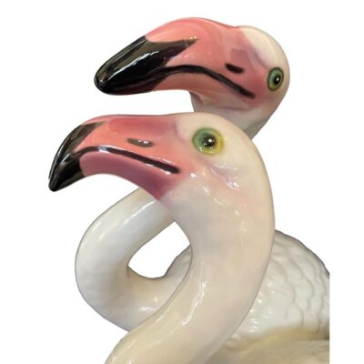 Italian made flamingo statuette. An eye catching ceramic statuette of a pair of flamingos stood together. These are Greater flamingo species. Marked Italy to the base. Close up photo of the birds heads. The bird in foreground is facing straight left and the taller bird in the background is looking towards camera with left eye only visible.