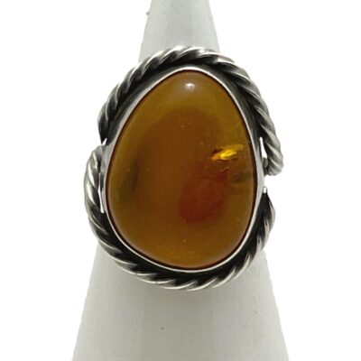 Vintage sterling silver ring with amber. Large statement ring with cognac amber set in sterling silver. Nice rope twist silver design starting at each shoulder and worked around the stone to top and bottom. Hallmark to the outside of band at back. Ring size N.5 / 7. Main photo of ring displayed on a cone shaped stand and seen with the ring front facing forward. The large amber is egg shaped.