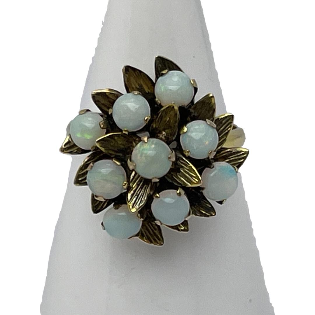 Vintage ring with fiery opals. Eye catching 14 karat gold ring set with 9 small fiery opals in the form of a floral bouquet. Lovely subtle flashes of colour in an otherwise milky opaqueness. Size N / 6.75. Weight 3.6grams. Main photo of ring displayed on a cone shaped stand with the ring front forward facing. The colours of the opals are barely visible and just appear to be milky white.