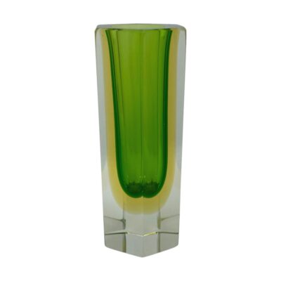 Main photo of vase seen from an eye level with the sommerso design fully visible. The inside layer is a fresh green colour which is hi-lighted with a yellow aura and finished with a clear glass outer layer and base. The image is like a small green round bottomed vase within a hexagonal clear glass vase with the green and clear glass vases separated with a lemon yellow band. The vase is posed with one point of the hexagon base in the foreground.