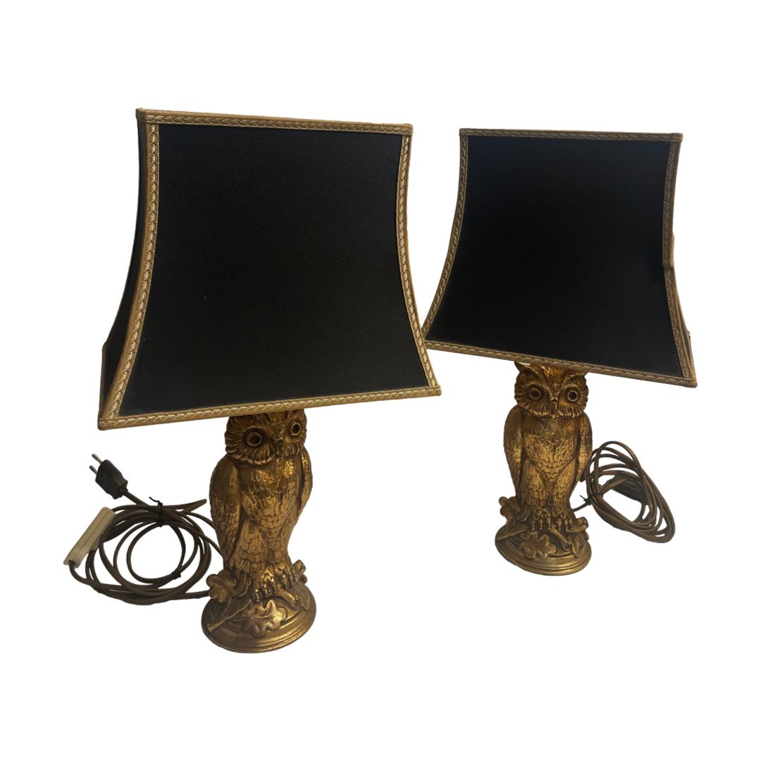 Pair of lamps in owl form with shades. Vintage pair of 1970s retro gilt metal owl lamps with black shades. The owls are perched on an oak branch with nice detailing to the owls features. The shades are gilt foil lined and in a matt black material to the outside. One shade has minor crease damage. The base measures 100mm in diameter and 270mm tall. The shades are 265mm at widest, 185mm at deepest and 225mm tall. Collect from store only. Main photo showing the 2 lamps together with the one on left slightly more to the foreground. The owls are both forward facing with the black almost bicorn hat like shades shown lengthways.