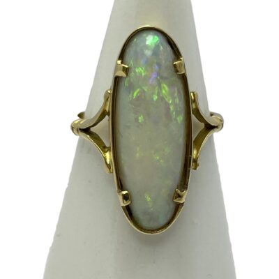 Main photo of ring displayed on a cone shaped stand. The ring front is forward facing. The opal is of a long oval shape and set on split band shoulders. The opal is a milky white with flashes of good colour. In this photo, there are flecks of yellow, green, lilac and pink.