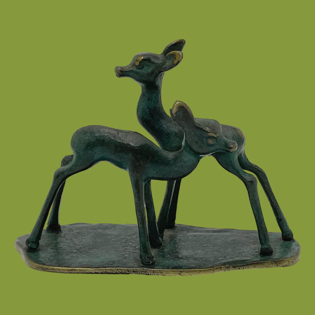 Main photo of deer seen from an eye level. They are displayed with the shorter one in the foreground facing right and taller in the background facing left. The deer are set against a fern green background which enhances the green patina of the metal.