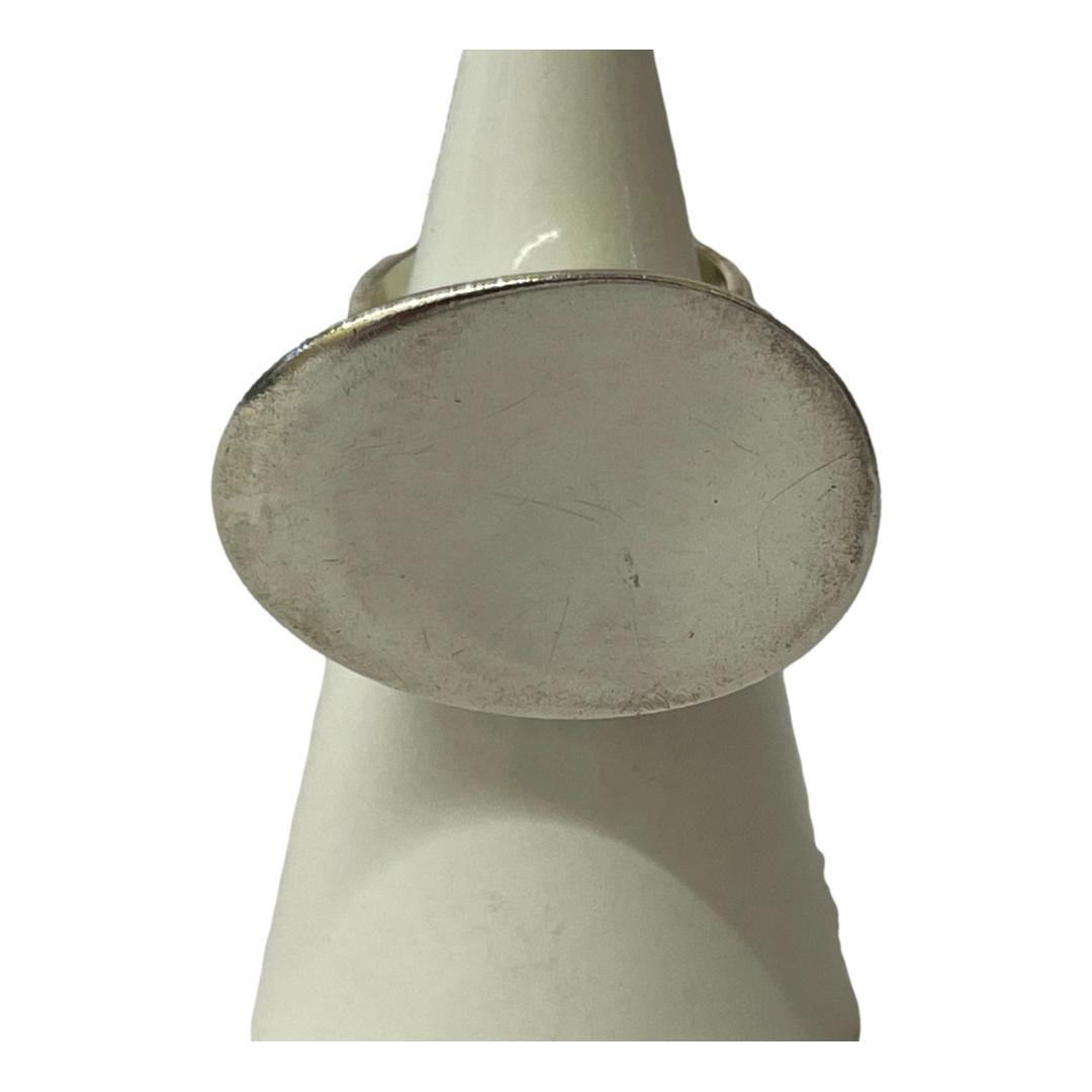 Main photo of Georg Jensen serenity ring displayed on a white cone shaped stand against a white background. The ring has a good sized concaved frontage which spreads out to the sides so wider horizontally. Owing to the white surrounds, the ring actually looks off white instead of the silver that it is. A very sought after and collectable ring.