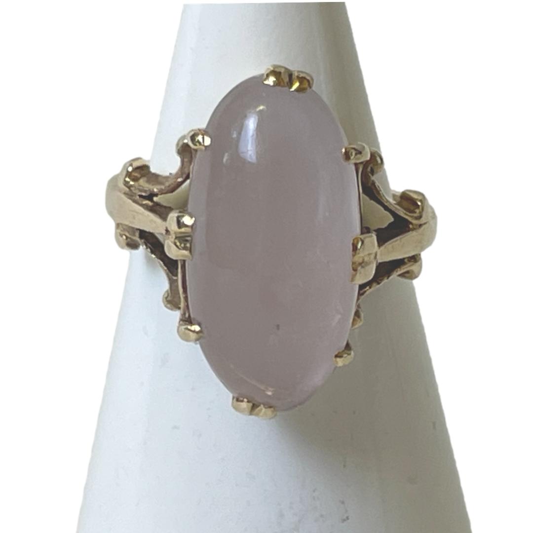 Main photo of 9kt rose quartz ring displayed on a cone shaped stand with the ring front forward facing. The rose quartz cabochon is a generous oval size and beautifully polished. It is securely clawed in place with double claws to the top, bottom and sides and additional single claws in between these.