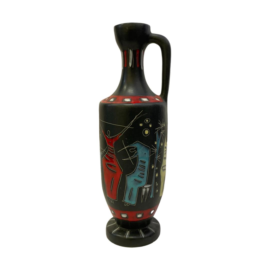 Main photo of 1960s Gianni Tosin jug displayed against a white background and from an eye level. The single handle is on the right. This jug is in a lovely matt black glaze with figures who appear to be playing music and dressed in vibrant red, blue and yellow with a fine horse in white. This is one of those the more you look the more you see pieces or amazing studio pottery.