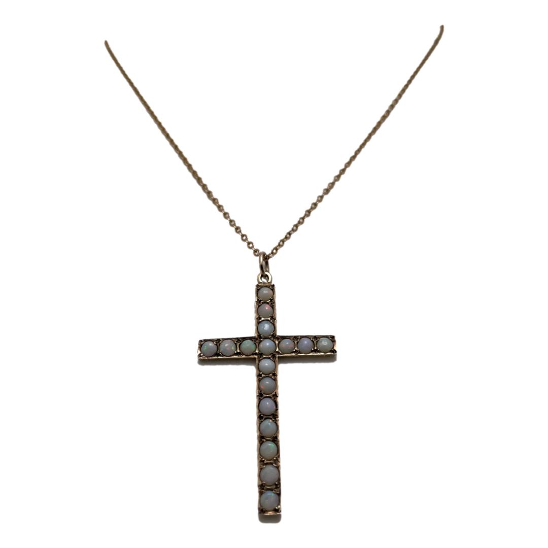 Main photo of 9kt opal cross &chain displayed on a stand which is not visible and focusing in on the cross. 11 opals are set vertically down the length of the cross with 3 each to either arm. The necklace is a fine chain which compliments the cross.