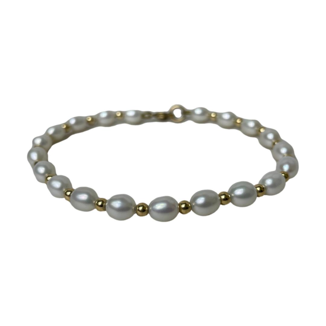 Main photo of 9kt gold & Pearl bracelet displayed on a flat surface and laid in a circle with the clasp closed. The pearls have a light grey hue and are oval in shape. Each pearl is separated with a gold bead.