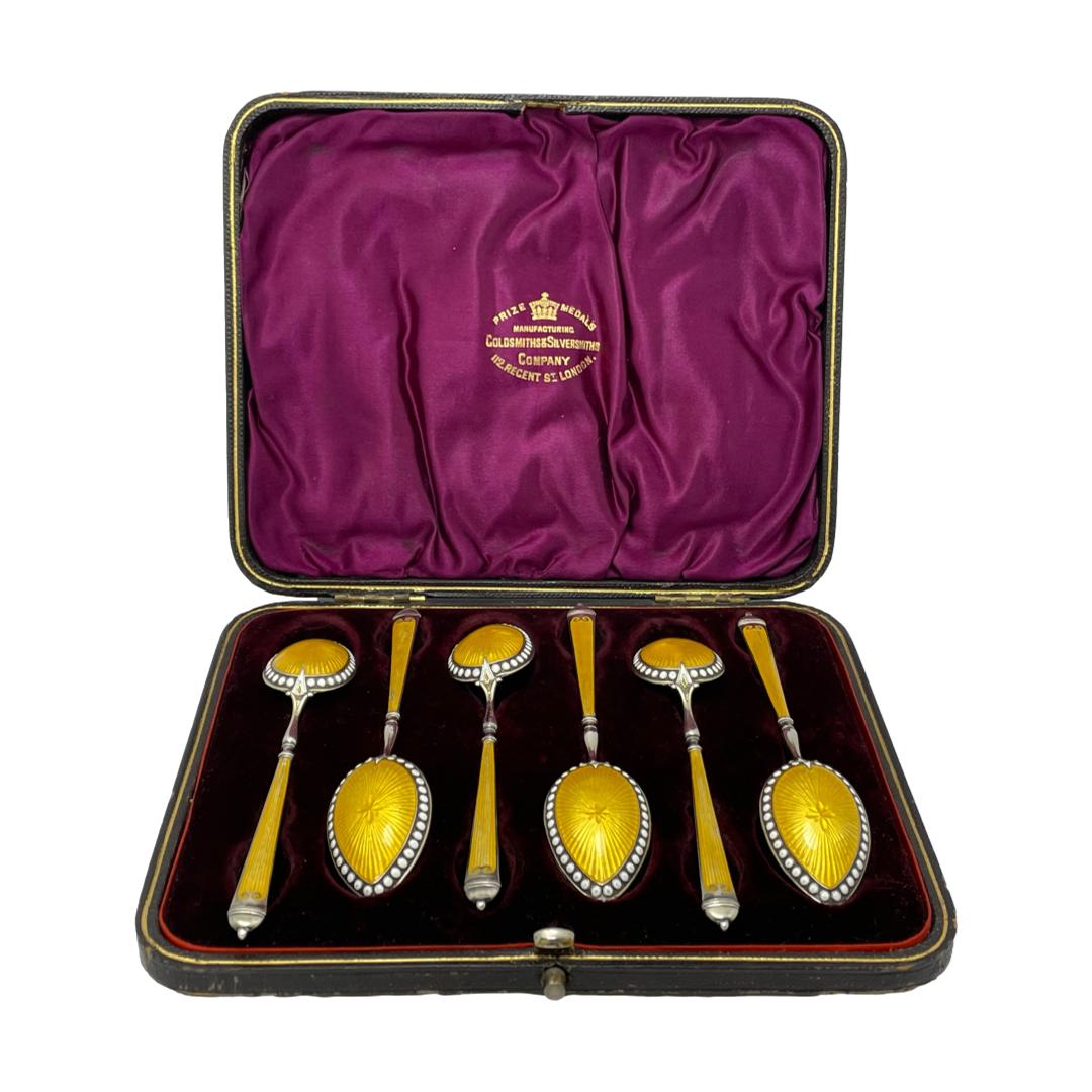 Main photo of silver yellow guilloche spoons displayed inside the fitted case with spoon bowls face down and displayed the guilloche enamel. The case is a deep wine colour with velvet fitted space and silk to inside lid. The case is not the original one but the spoons fit perfectly well and the Goldsmiths and Silversmiths logo on the inside lid in gold compliments the whole esnsemble.