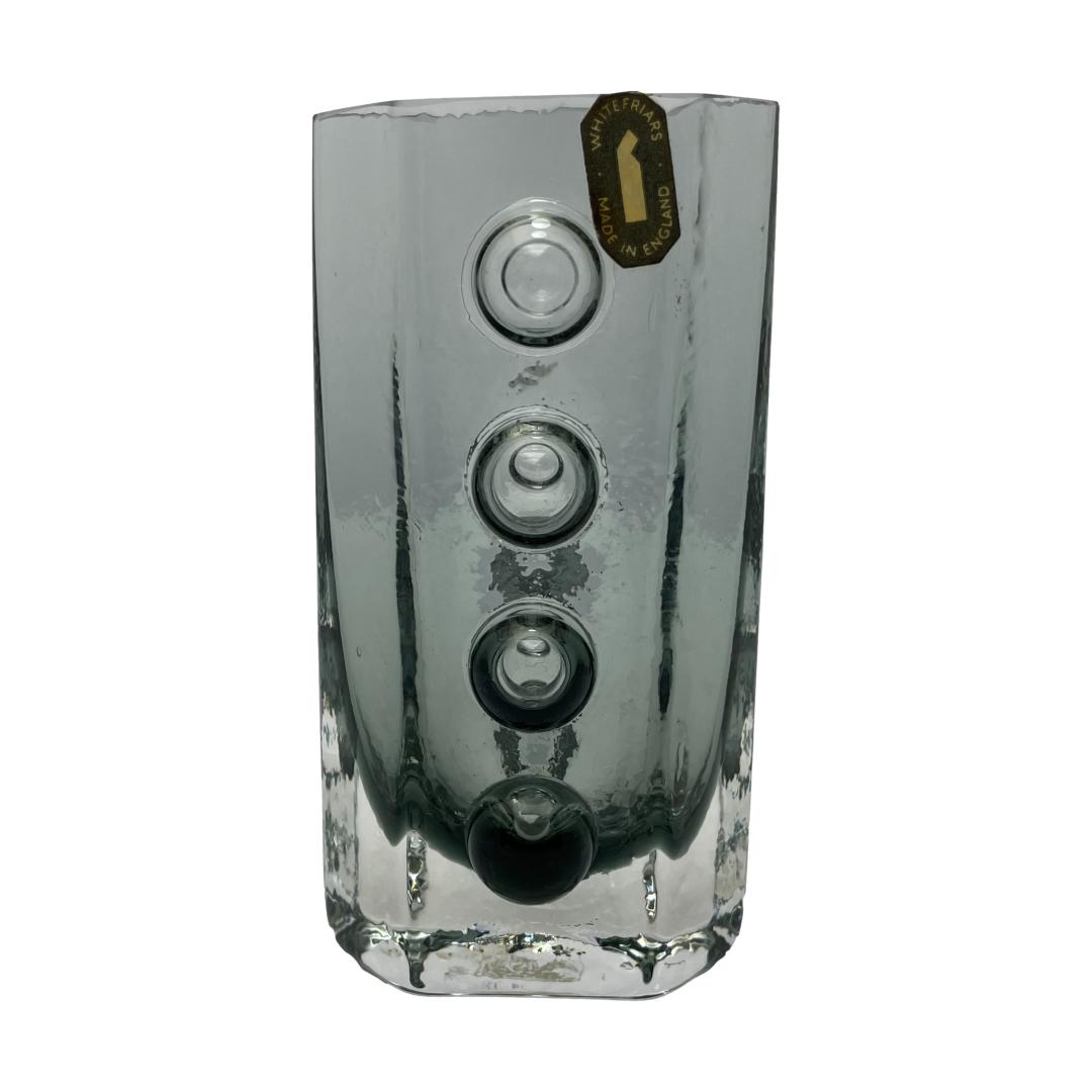 Main photo of Whitefriars traffic light vase shown with one traffic light side on display. The 'lights' are 3 circles of glass vertically aligned which are protruding from the main body of vase. Lovely solid & stylish little vase synonymous with the Whitefriars name.