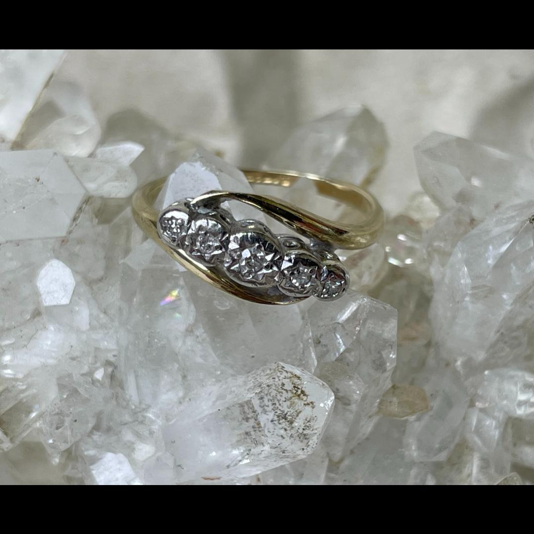 Main photo of gold platinum diamond ring displayed on top of a rock of natural quartz crystal and seen with ring front facing forward. The gold band is split with each end curved over the diamonds which are set in platinum at the centre.