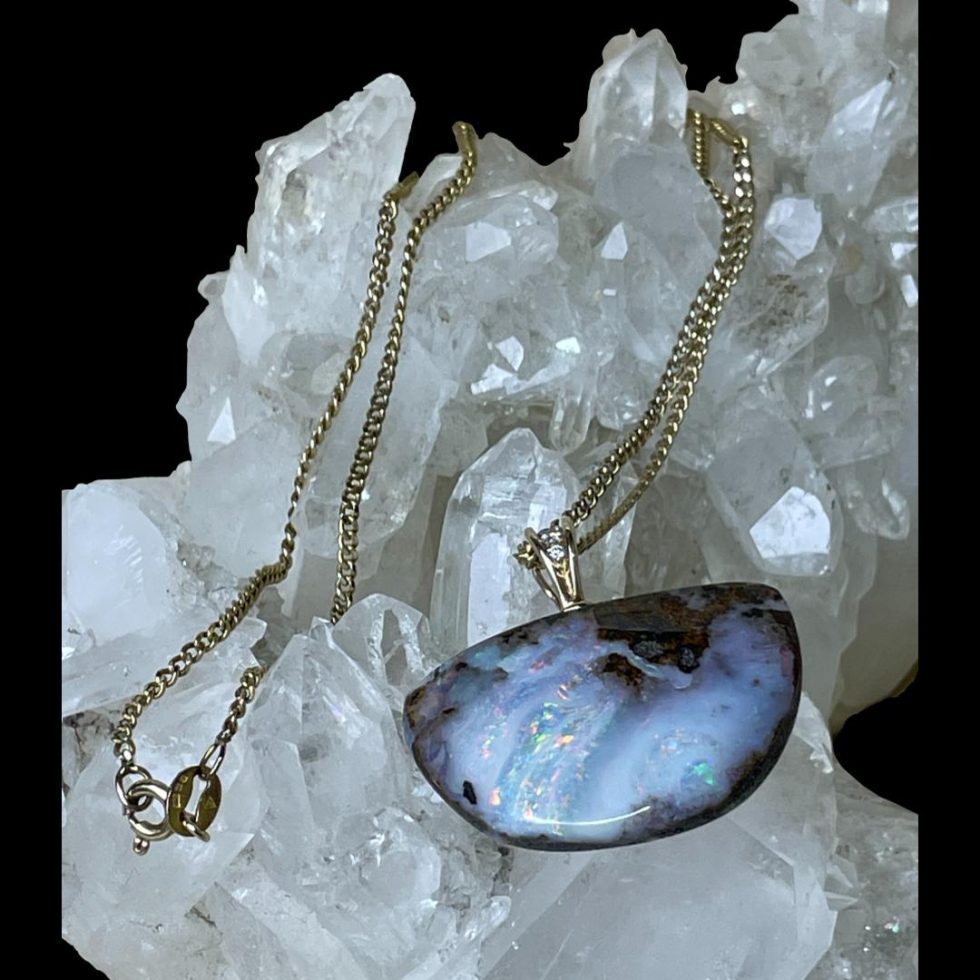 Main photo of boulder opal &diamond necklace displayed on top of a rock of natural quartz crystal. The pendant is to the lower right with the front on view. This is a lovely natural opal stone set in pendant form with a diamond in the bail. The gold chain has been draped over the crystal.