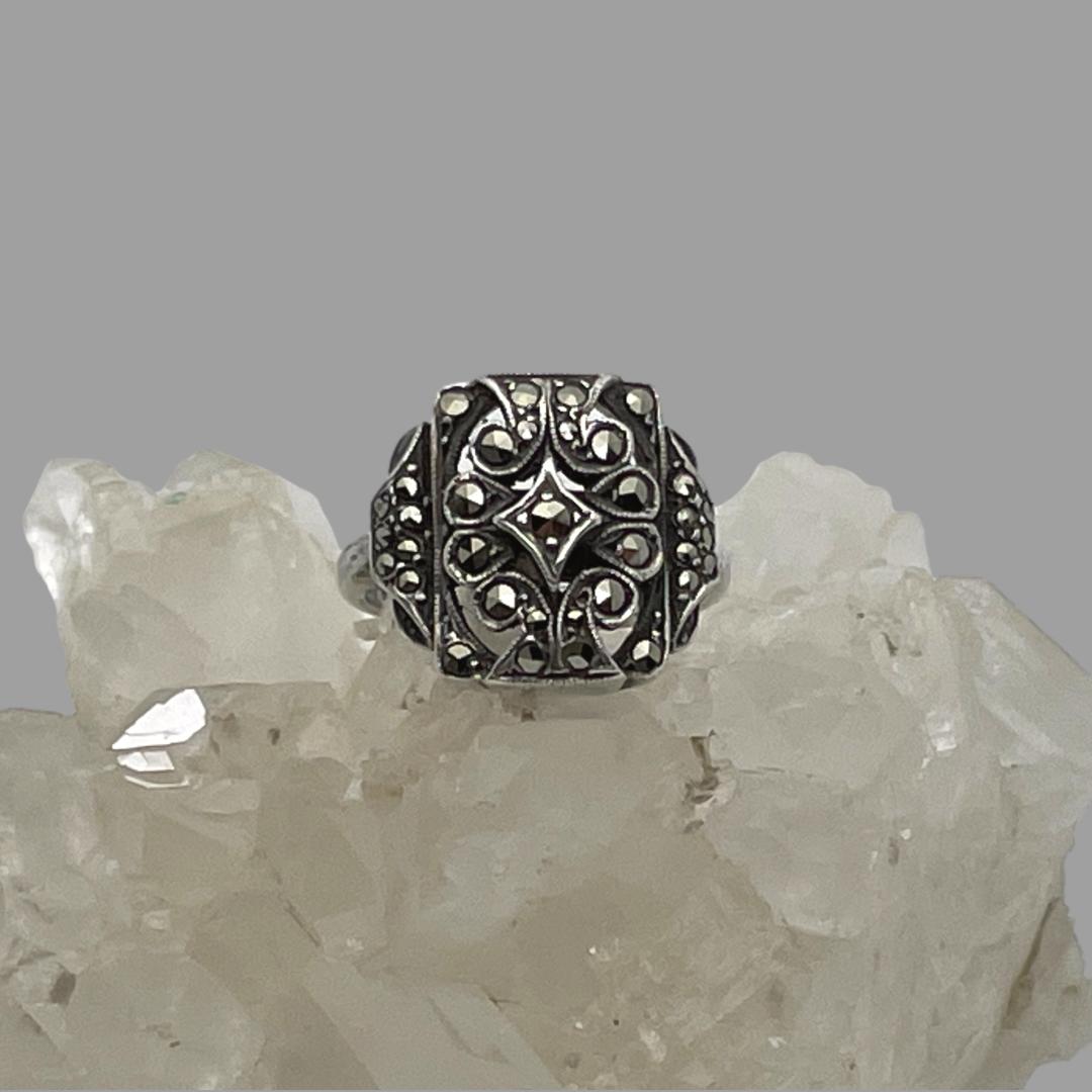 Main photo of adjustable silver marcasite ring displayed on top of a rock of natural quartz crystal with the ring front forward facing. The ring has a minimalist design of a squarish front with different shapes within.