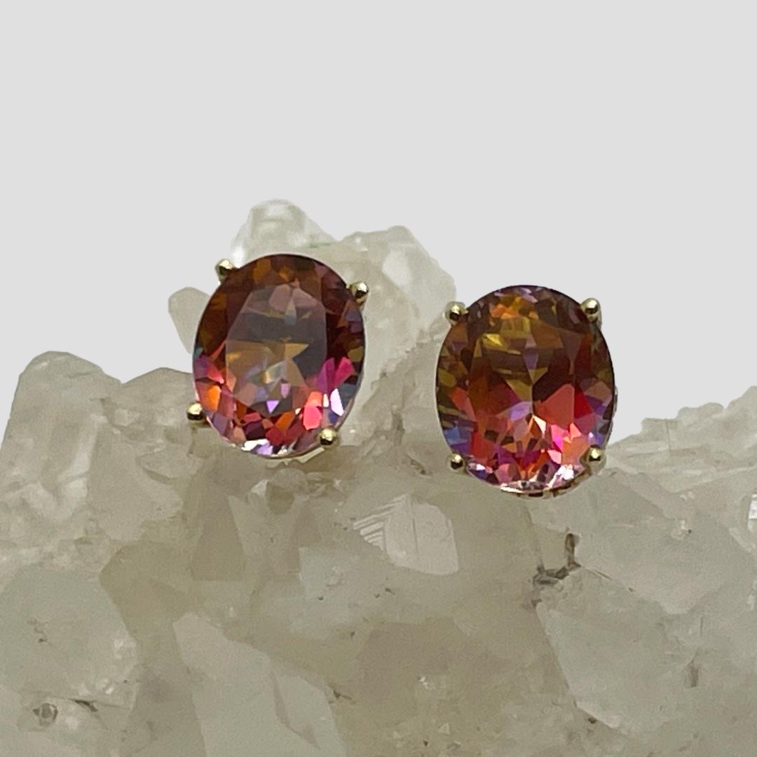 Main photo of mystic topaz 14kt studs displayed on top of a rock of natural quartz crystal with the earrings forward facing. The colours from these stones is amazing, in this photo they are primarily pink with orange and lilac flashes.