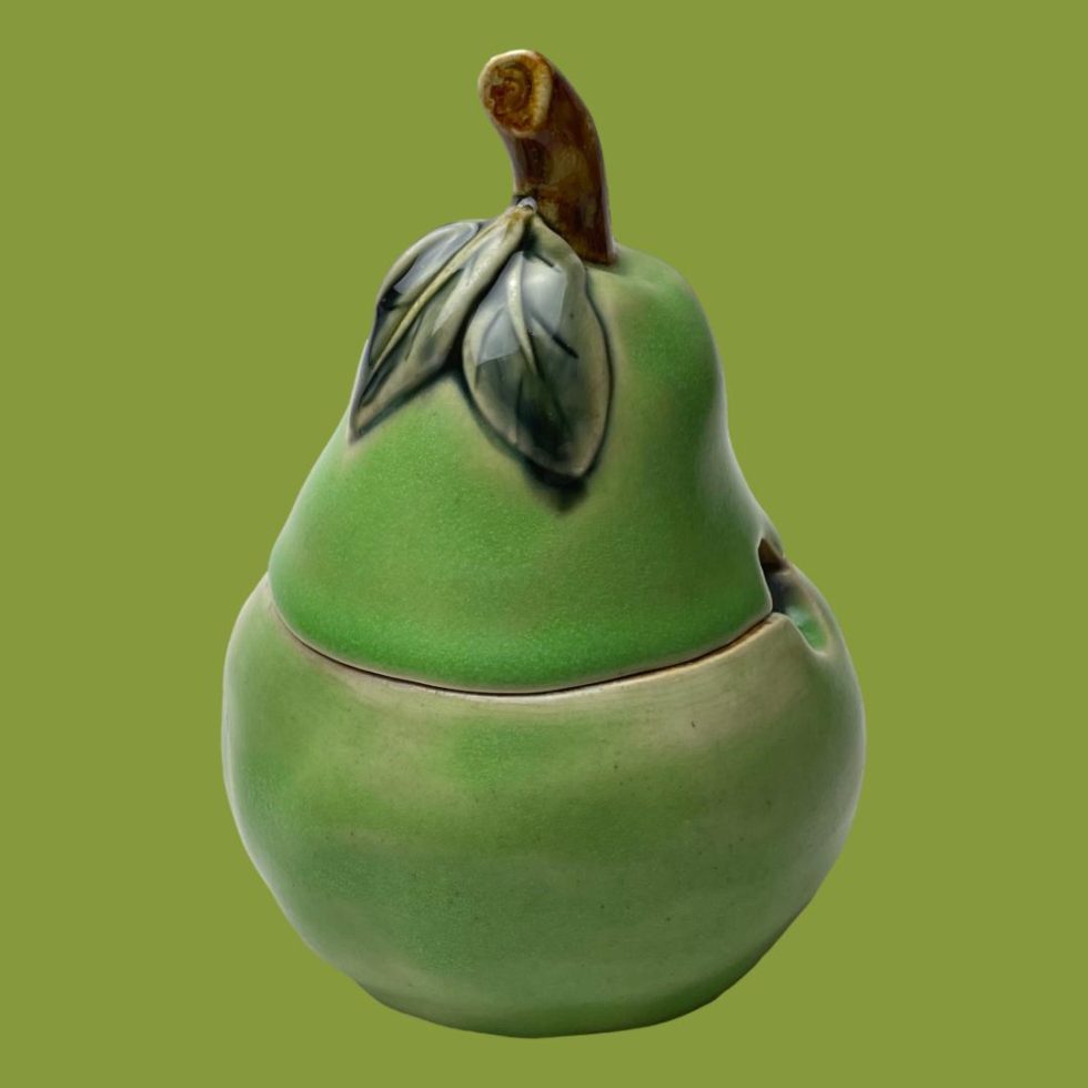 Main photo of Doulton pear preserve pot seen from an eye level. The pear is a green colour with short brown stalk ad 2 darker green leaves at the top. The lid is proportionate to the bottom half.