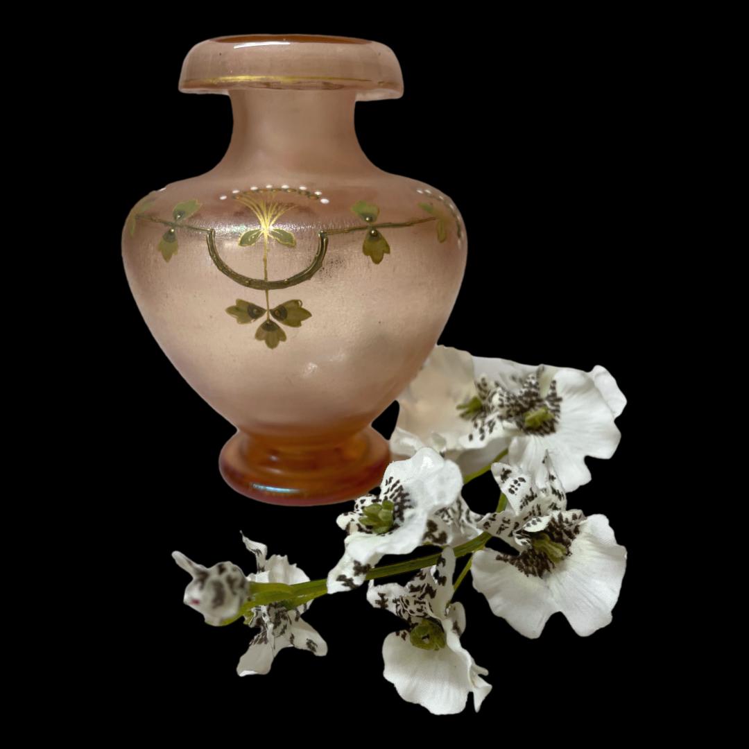 Main photo of Nouveau iridescent glass vase seen with main decorative side on display The pale peachy pink glass is thicker and more iridescent at the base and lip of the vase. At the centre of the decoration is a stylised dandelion head with gold dot in centre then gold sprayed out followed by a circle of gold dots then a circle of white dots. Above the central head are 2 side view heads to the left and right above the central one. Very simplistic design but incredibly effective. A spray of white orchids is seen to the right hand side of vase for decorative purposes.