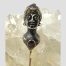 Main photo of Austro-Hungarian tie/stick pin showing the top part of the pin which has the bust of the lady. She has a tight fitting turban like hat on with an amethyst to the centre and amethyst eyes. She is also wearing a necklace with a large carnelian cabochon. The turban has gilt and silver stripes and she is wearing a gilt gown although only the neckline area can be seen. She has a strange look about her face like she is a little crazed or drunk - a very quirky piece indeed!